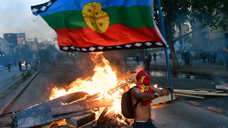 Un manifestant tient un drapeau devant un feu de débris dans une rue de Santiago.