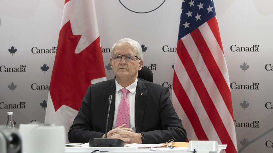 Marc Garneau devant un drapeau canadien et américain.
