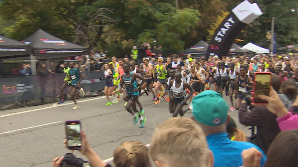 Un flot de coureurs, devant des spectateurs qui prennent des photos.
