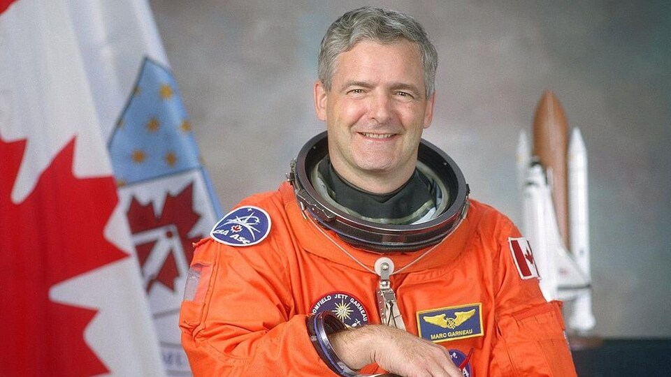 L'astronaute Marc Garneau devant le drapeau canadien.
