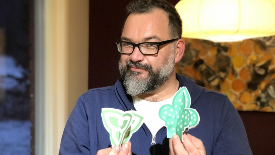 L'artiste tient dans ses mains deux décorations en papier vert et blanc.