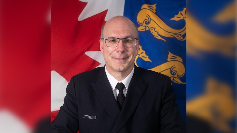 Un uomo in uniforme posa davanti a una bandiera canadese