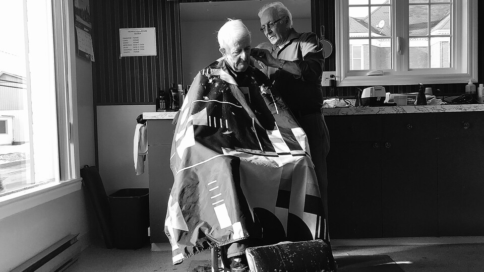 Un barbier de 76 ans coiffe un homme âgé.