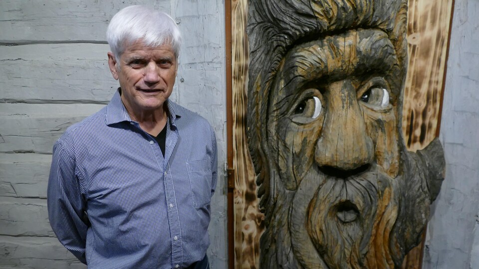 Marcel Ritchot est debout devant la sculpture de bois.