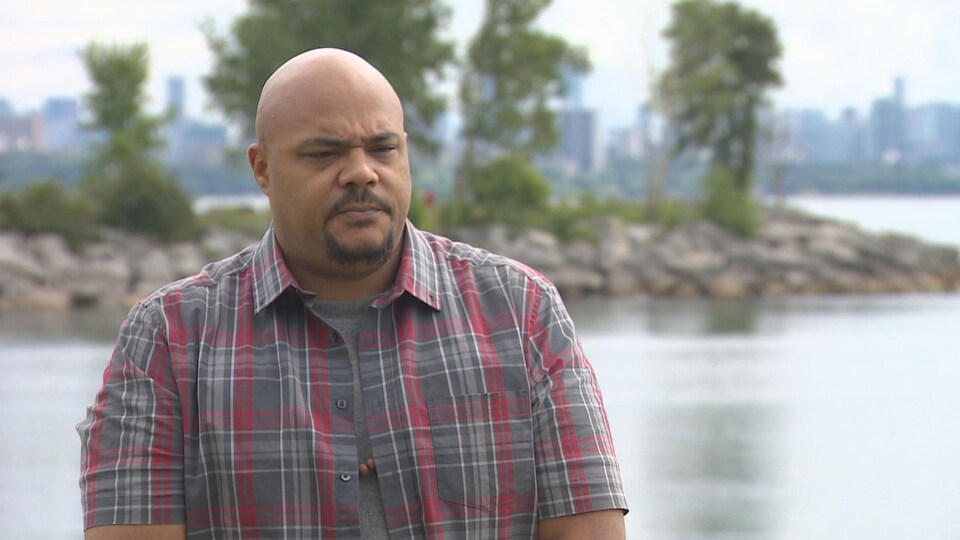 Un homme debout à l'extérieur devant un lac. Au loin, la vue du centre-ville de Toronto.