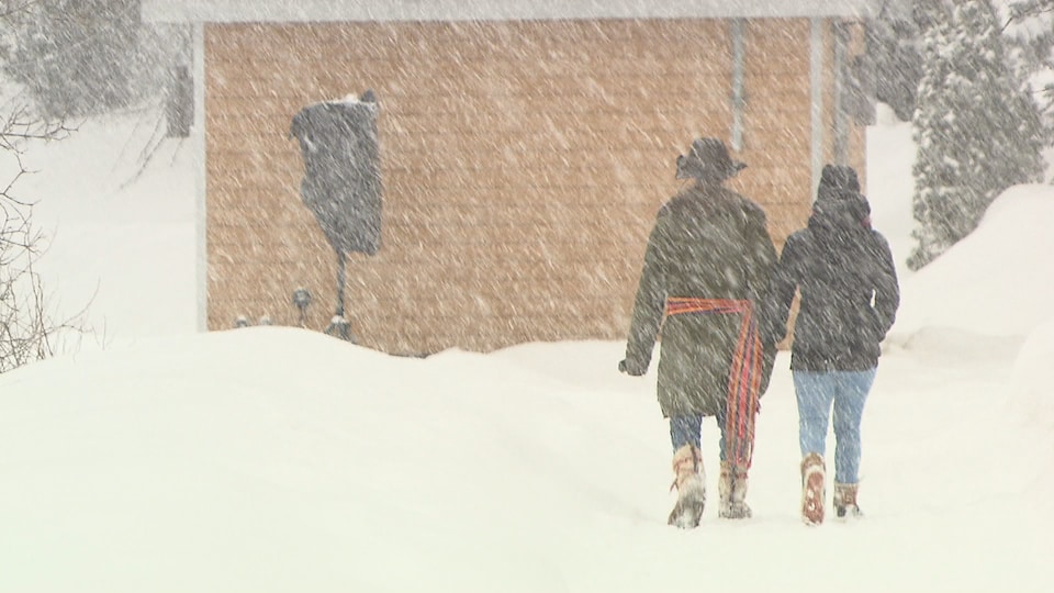Deux personnes marchent main dans la main sous la neige. L'une porte un foulard orange, rouge et mauve à la taillle. 