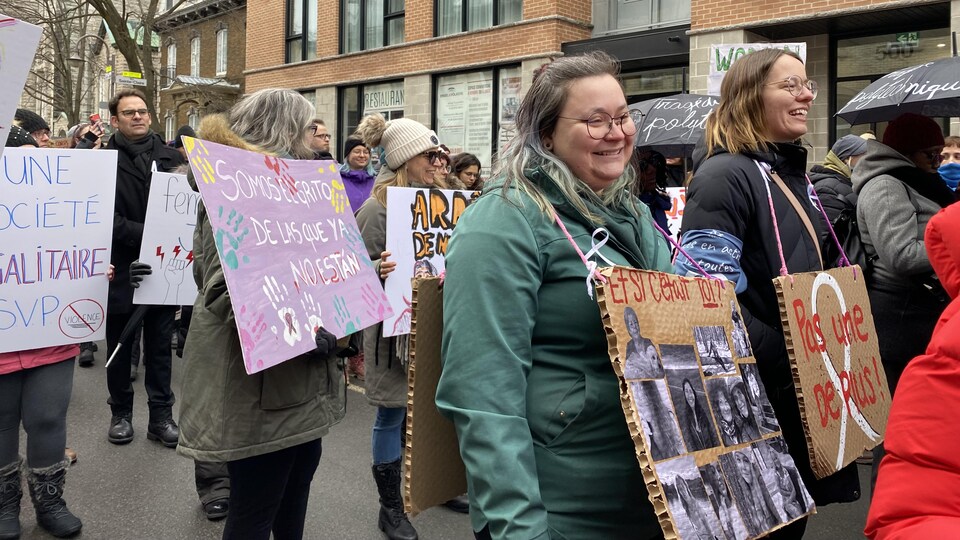 Des femmes marchent dans la rue, des pancartes au cou, en souriant. 