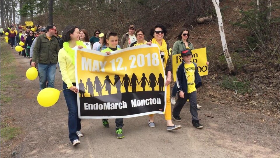 Marcheurs avec une affiche jaune et noire annonçant leur marche pour la sensibilisation à l’endométriose.