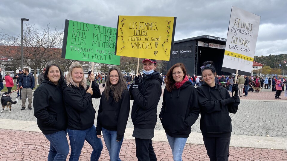 Six femmes montrent leur pancarte. Elles sont devant la place du citoyen à Saguenay.