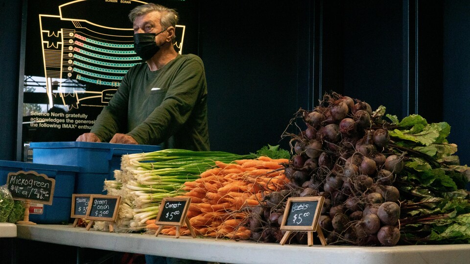 Un fermier debout derrière une table où on peut voir des radis et des carottes.