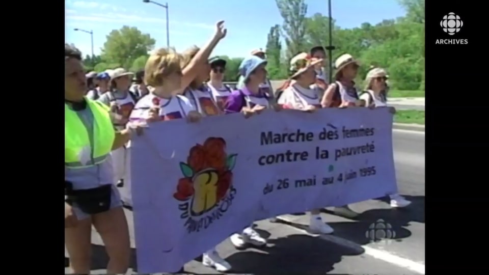 Femmes qui avancent en tenant une banderole avec l'inscription "marche des femmes contre la pauvreté".