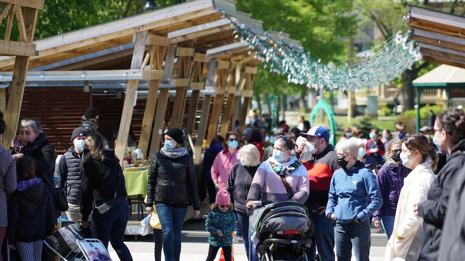 Des gens portant le masque marchent sous le soleil au Marché public de Rimouski.