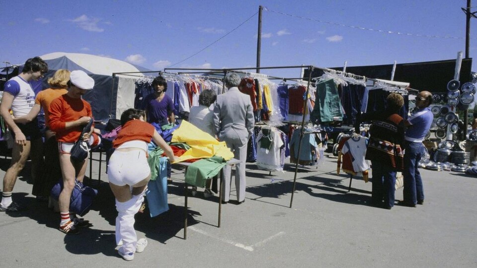 Clients devant un kiosque de vêtement au marché aux puces Saint-Hippolyte.