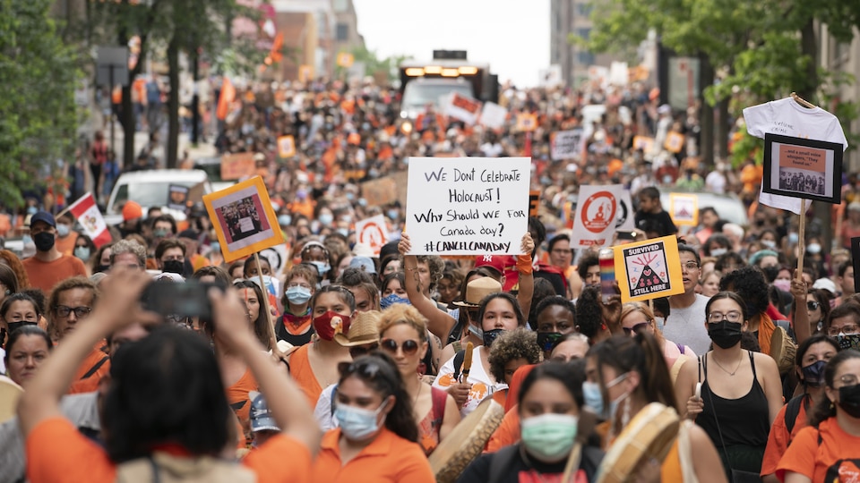 Des milliers de personnes dans les rues, dont plusieurs portent un chandail orange ou ont une pancarte. 