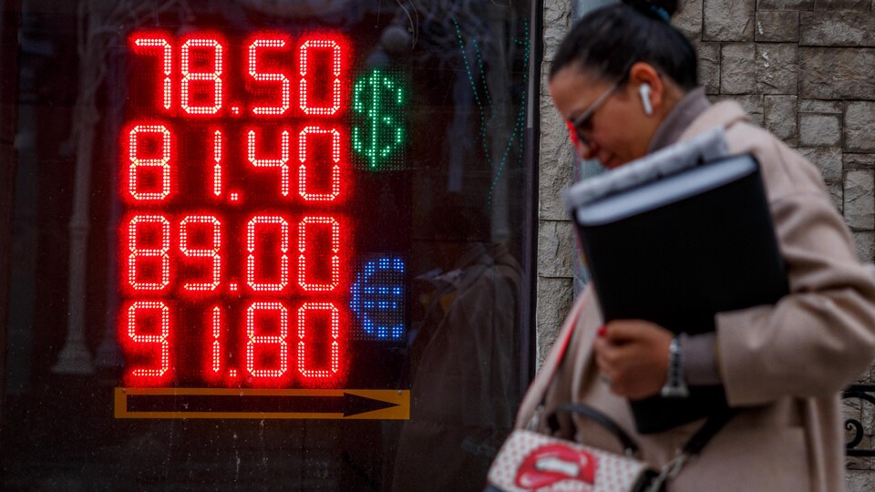 Une femme marche devant une affiche lumineuse sur laquelle sont indiquées la valeur du rouble et celle du dollar.