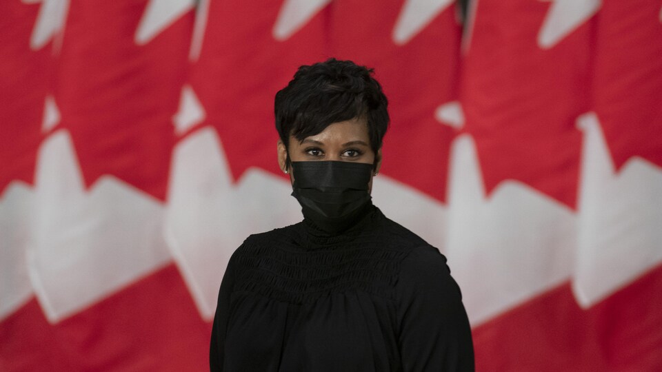 Une femme portant un couvre-visage devant plusieurs drapeaux du Canada.
