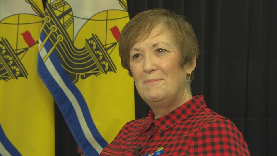 La ministre, souriante, lors de l'entrevue. Elle est assise devant deux drapeaux de la province. 