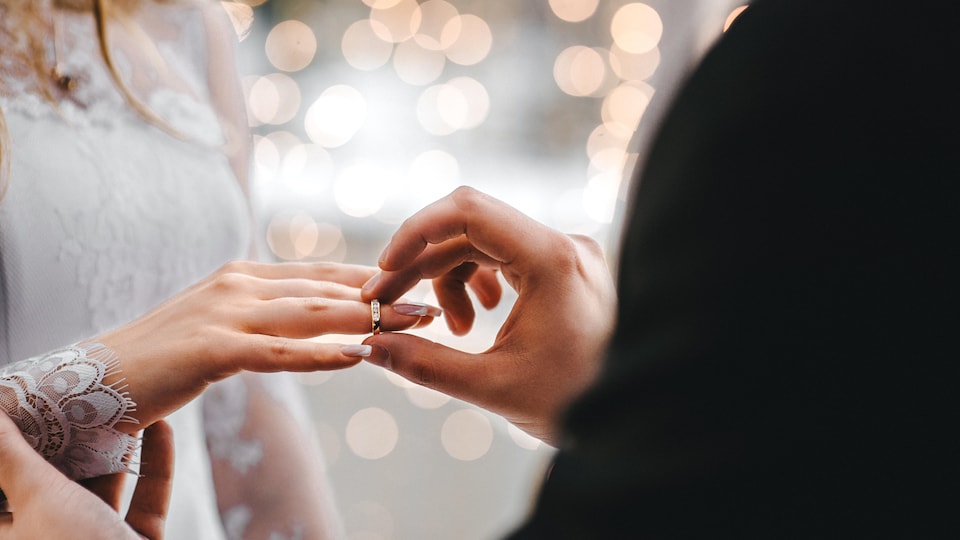 Deux mains de mariés dont l'une échange une bague à l'autre.