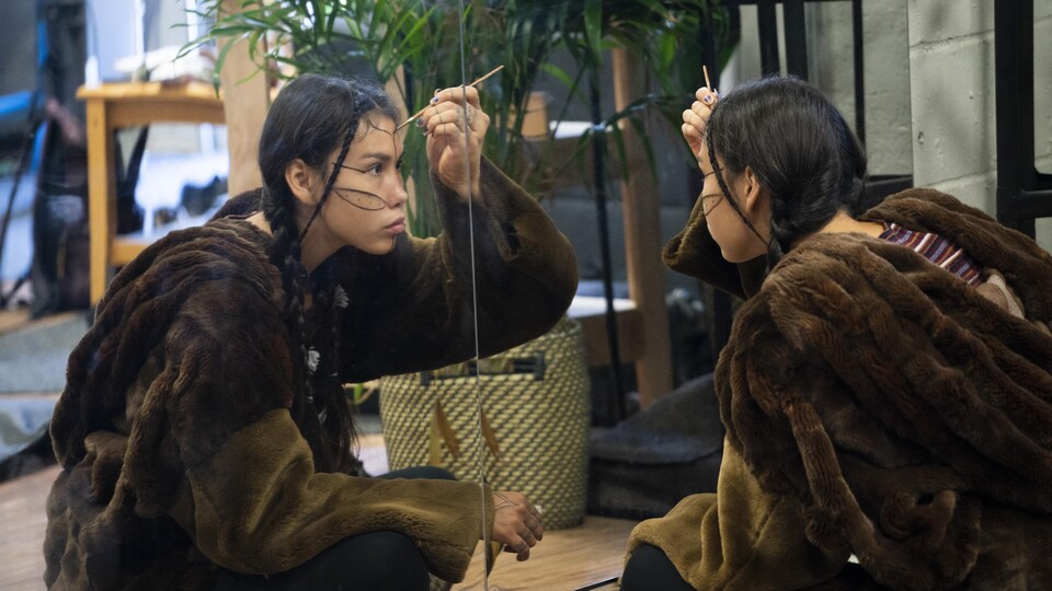 Mariam Imak qui se maquille devant un grand miroir.