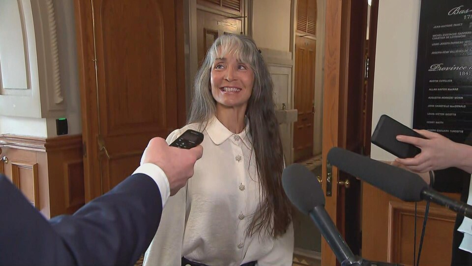Marie-Louise Tardif devant des micros dans un couloir.