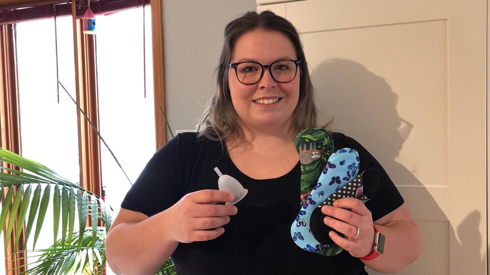 Une femme tient dans ses mains une coupe menstruelle et des serviettes hygiéniques lavables.