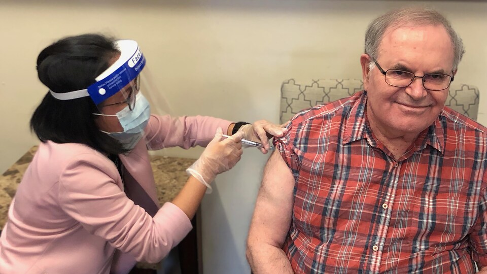 Un homme se fait vacciner par une infirmière. Il sourit.
