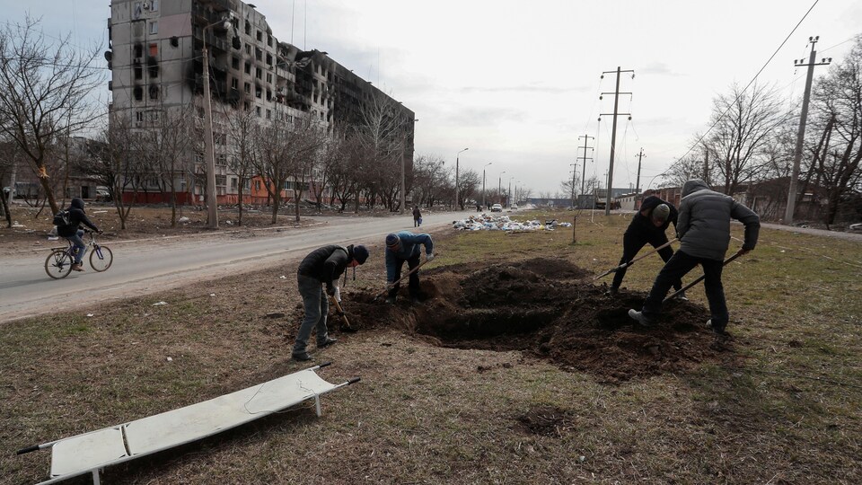 Quatre hommes creusent des tombes près d'une route.