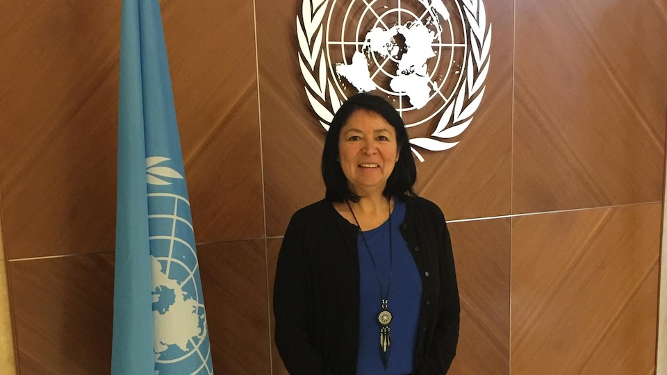 Une femme autochtone pose devant un logo et un drapeau de l'ONU.