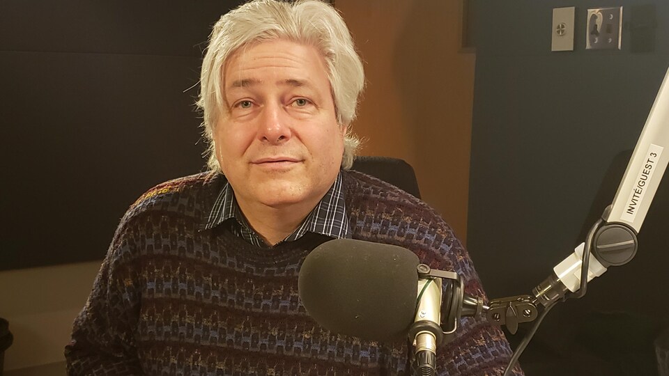 Un homme aux cheveux grissonnant souriant dans un studio de radio. 