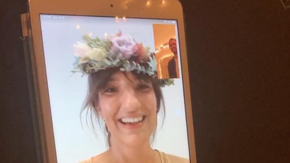 Une femme porte une couronne de fleurs sur les cheveux et appelle son conjoint par vidéoconférence.