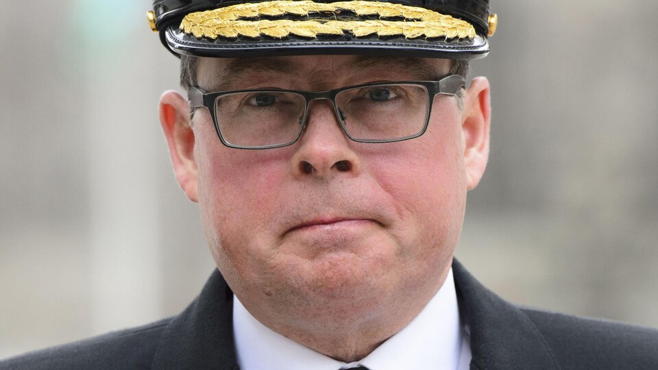 Gros plan sur le visage du vice-amiral des Forces armées canadiennes Mark Norman qui porte un képi militaire et des lunettes.