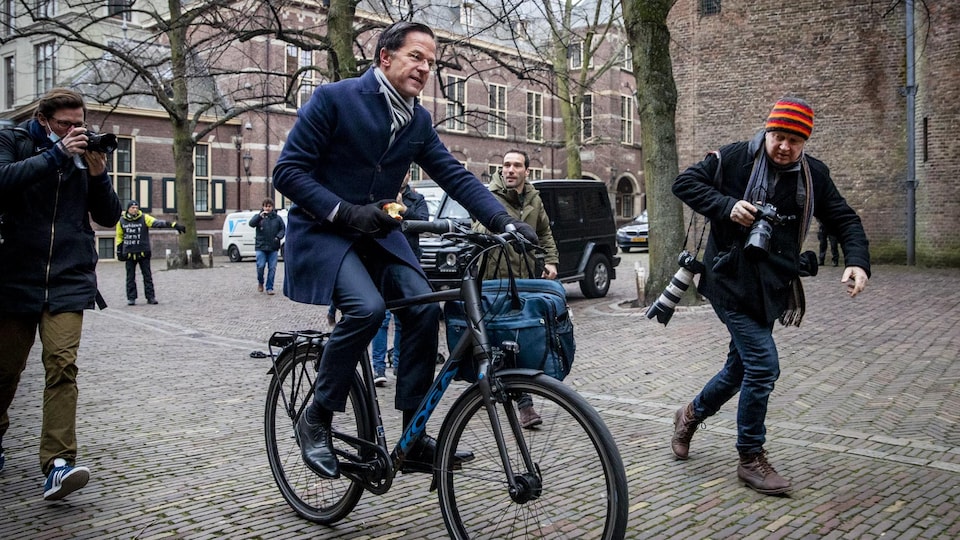Mark Rutte est pourchassé par des photographes alors qu'il circule à vélo, une pomme en main.
