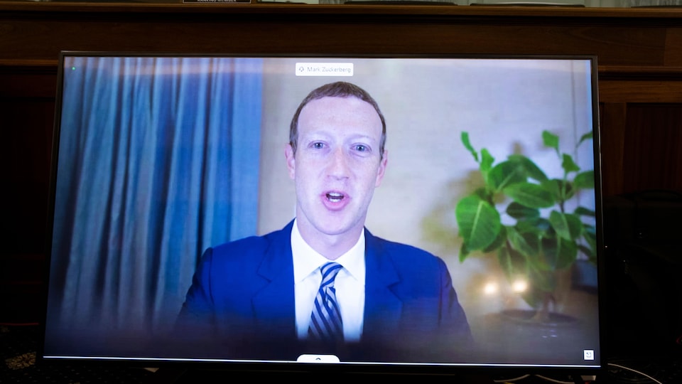 Un homme en veston cravate apparaît de face sur un écran d'ordinateur. 