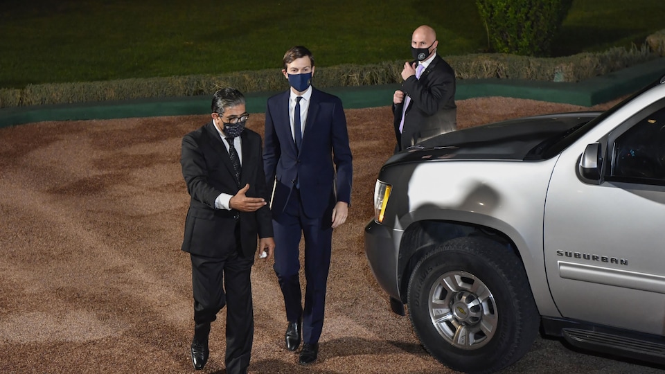 Trois hommes dans un jardin devant une voiture stationnée.