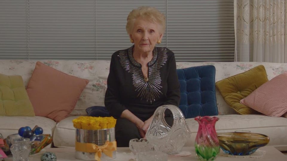 La femme est assise sur un sofa et regarde devant elle.