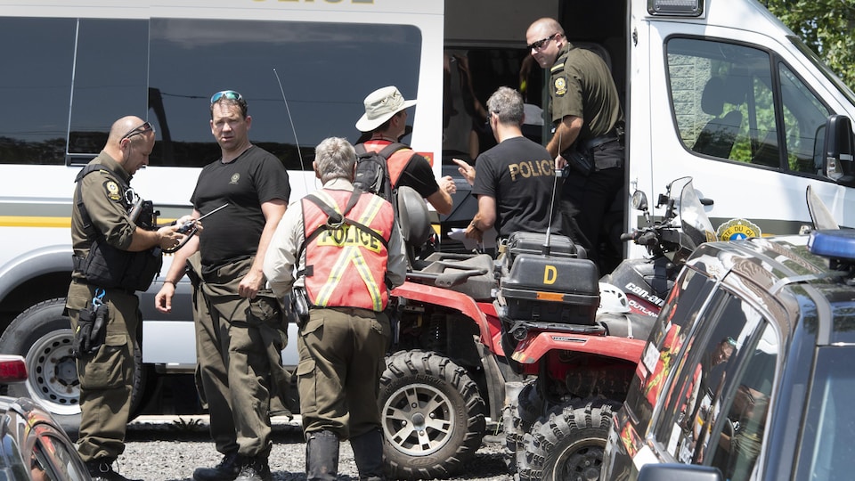 Six policemen were talking near a police car and an ATV.
