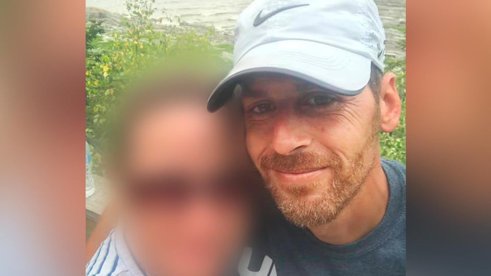 Martin Carpentier porte une casquette blanche de marque Nike. Il a une petite barbe aux teintes de roux, les cheveux bruns ainsi que les yeux bruns.