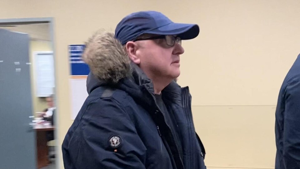 Le quinquagénaire porte une casquette et des lunettes.