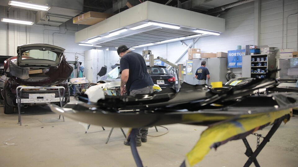 Deux hommes de dos dans un atelier de mécanique automobile. 