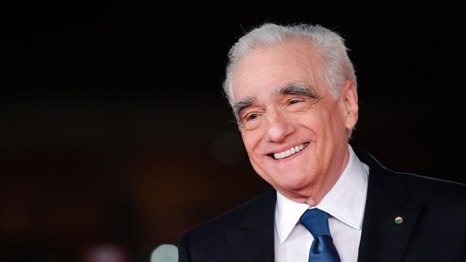 Martin Scorsese sourit et porte un complet sombre ainsi qu'une cravate bleue. 