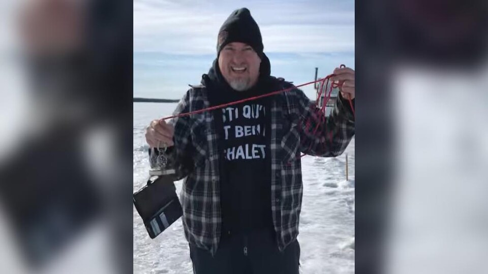 Martin Turbide tient fièrement un fil avec un aimant sur un lac gelé. Au bout, le cellulaire de sa conjointe dans un étui avec des pièces d'identité.