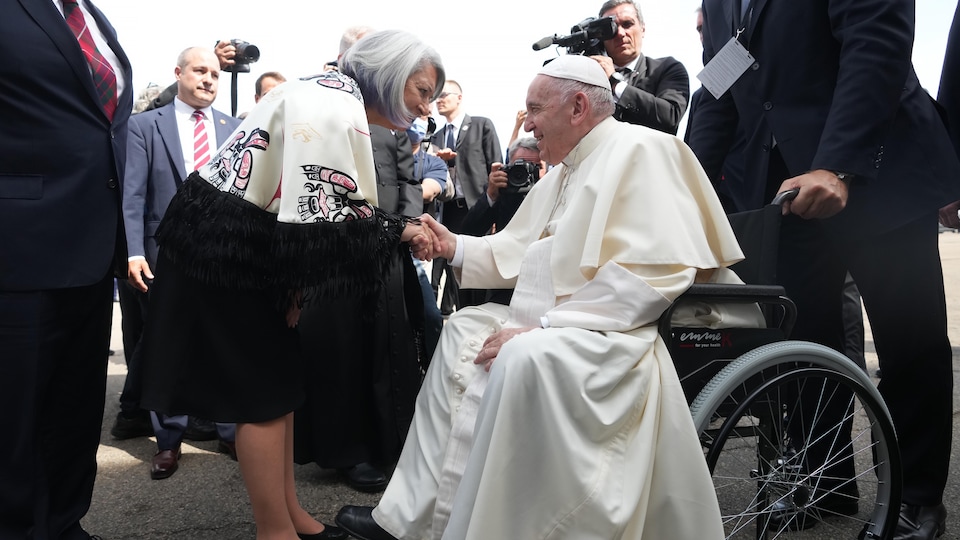 La gouverneure générale serre la main du pape, qui est assis dans une chaise roulante. 