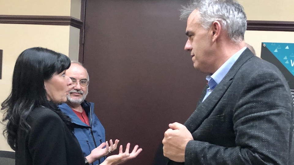 Une femme discute avec un homme qui lui fait face tandis qu'à sa gauche, un homme écoute la conversation.