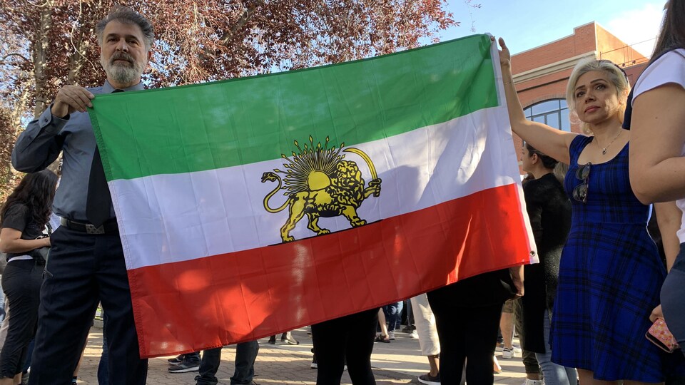 Shahab Shakeri tient le drapeau iranien avec l’emblème de la Perse royale à Calgary, 25/09/2022.