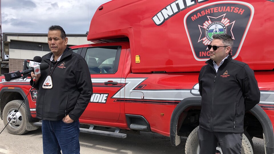 Two men were standing in front of a fire truck.