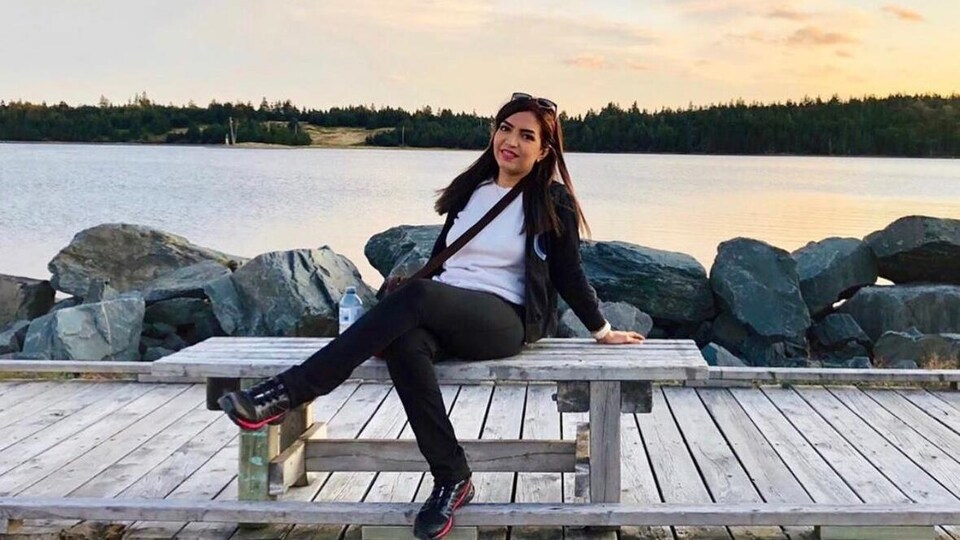 Une femme sur un banc en bois devant un lac.