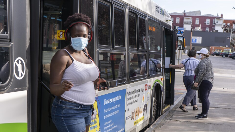 Une femme portant un masque descend d'un autobus.