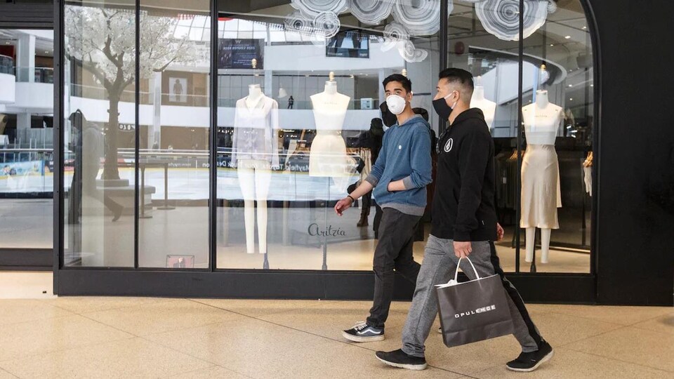 Deux jeunes se promènent dans un centre commercial et portent un couvre-visage.