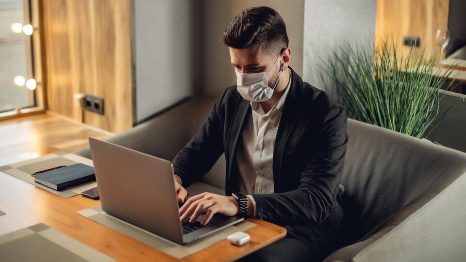 Un homme se sert de son ordinateur portable en portant un masque chirurgical.