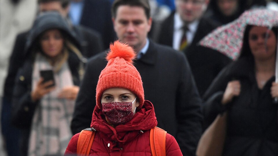 Une femme dans la foule avec une tuque à pompon et un masque rouge couvrant sa bouche et son nez.